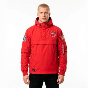 May include: A bright red hooded jacket with the NASA logo on the chest and an American flag patch on the sleeve. The jacket has a front pocket and a small patch on the other sleeve. The jacket is worn over black pants.