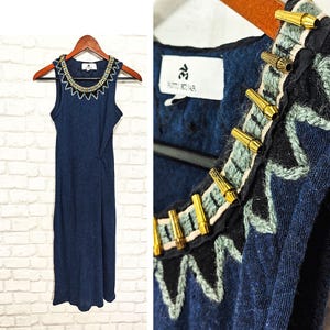 Könnte beinhalten: Ein ärmelloses Kleid in Marineblau mit einem goldenen und blauen Perlenbesatz am Ausschnitt. Das Kleid hat ein schlichtes, elegantes Design und ist perfekt für einen lässigen oder semi-formellen Anlass.