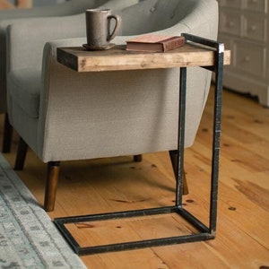 May include: A side table with a wooden top and black metal frame. The table is next to a light gray armchair with a cup and saucer on the top.