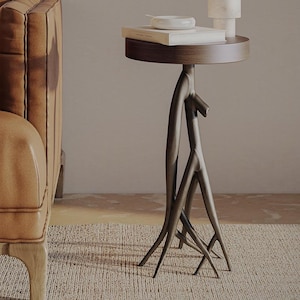 May include: A round wooden side table with a unique, branch-like metal base. The table is decorated with a white ceramic bowl and a stack of books.