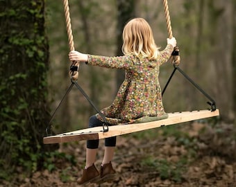 May include: A wooden swing suspended by thick, natural-fibre ropes features a rectangular seat with black metal brackets. The swing is designed for outdoor use, showcasing a sturdy, minimalist construction that hangs from above.
