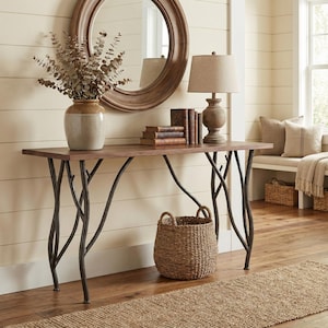 May include: A wooden console table with a dark brown top and metal branch-like legs. A woven basket sits beneath the table. A vase with dried branches, a lamp, books, and a mirror are on the table.