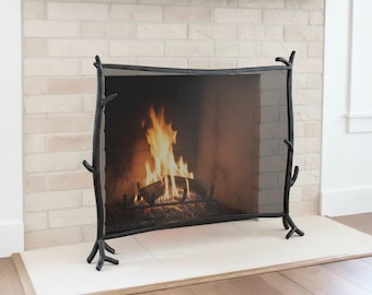 May include: Black metal fireplace screen with a branch-like design. The screen is in front of a fireplace with a burning fire. The screen has a rectangular mesh and is supported by four legs.