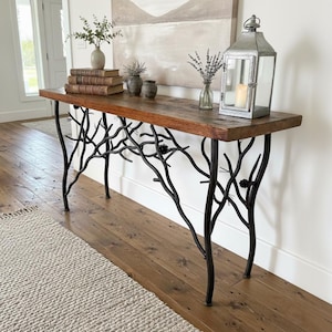 May include: A rustic console table with a dark wood top and black metal branch-like legs. The table is decorated with books, vases, and a lantern. The table is 60 inches long.