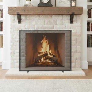 May include: A fireplace with a burning fire behind a black metal screen. The fireplace is set in a white brick wall with a wooden mantel and a white stone hearth. Bookshelves are on either side of the fireplace.