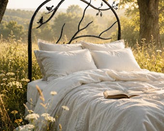 May include: A black metal headboard featuring a curved frame shaped like tree branches with small metal birds and leaves attached. The bed is dressed in white linen bedding with two pillows and an open book resting on the duvet cover.