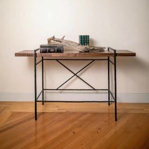 May include: A wooden console table with a dark metal frame. The tabletop is made of dark wood and has a natural wood grain. The table is decorated with books and driftwood. The table is 48 inches long, 16 inches wide, and 30 inches high.