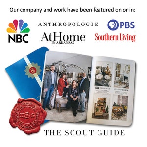 An open magazine with a blue cover and a red wax seal. The magazine is titled 'The Scout Guide'. The magazine features a photo of four people standing in front of a store with the name 'AtHome' and the text 'In Arkansas'. The magazine also features photos of home decor items and the text 'GRO', 'SING DESIGN CO', and 'URBAN FORGE'.