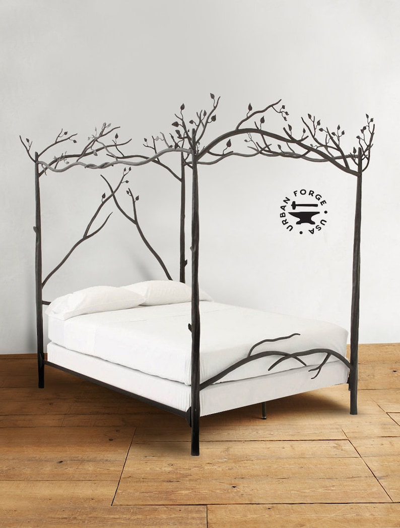 A black hand forged canopy bed frame with a white mattress. The bed frame is designed to look like tree branches with leaves.