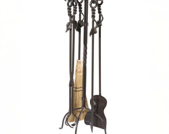 May include: A wrought iron fireplace tool set with a stand. The set includes a poker, shovel, tongs, and a broom. The tools have decorative leaf and twist designs. The stand has a circular top and three legs.
