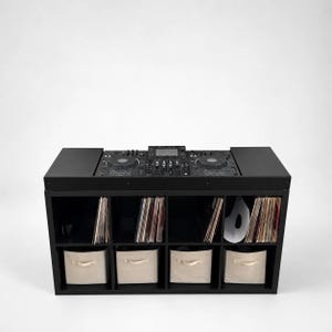 May include: A black DJ console station featuring a top-mounted mixer and dual jog wheels. The base is a black eight-cube storage unit with vinyl records organized in the top four compartments and four beige fabric storage bins in the bottom row.