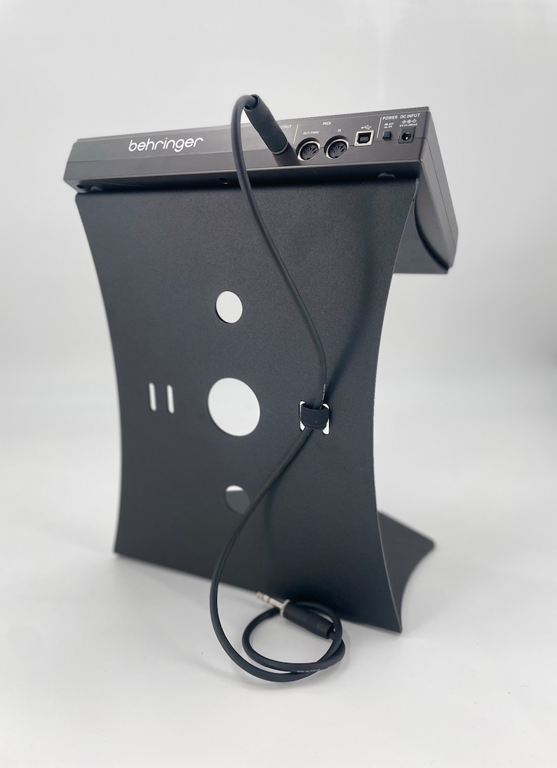 Op de afbeelding: Zwarte Behringer audio-interface met een zwarte standaard en een zwarte audiokabel die aan de achterkant is aangesloten.