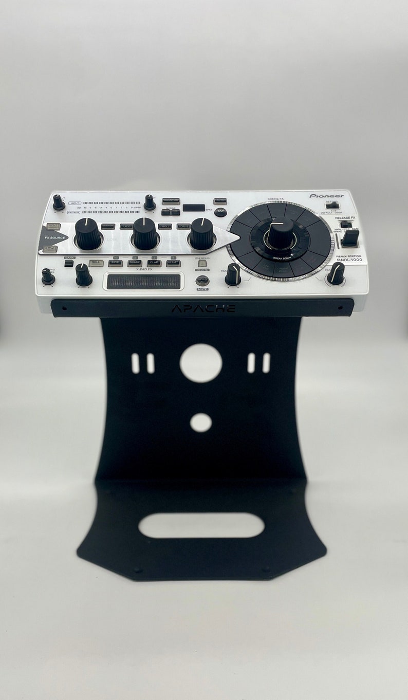 Op de afbeelding: Een witte Pioneer DJ-mixer met een zwarte standaard. De mixer heeft een grote centrale knop en verschillende kleinere knoppen en knoppen. De standaard is gelabeld "APACHE".