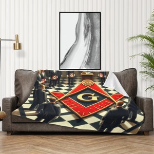 May include: A throw blanket featuring a Masonic emblem in red and gold, draped over a brown leather sofa. The blanket's design includes a checkered floor pattern and figures in suits. A framed abstract artwork hangs above.