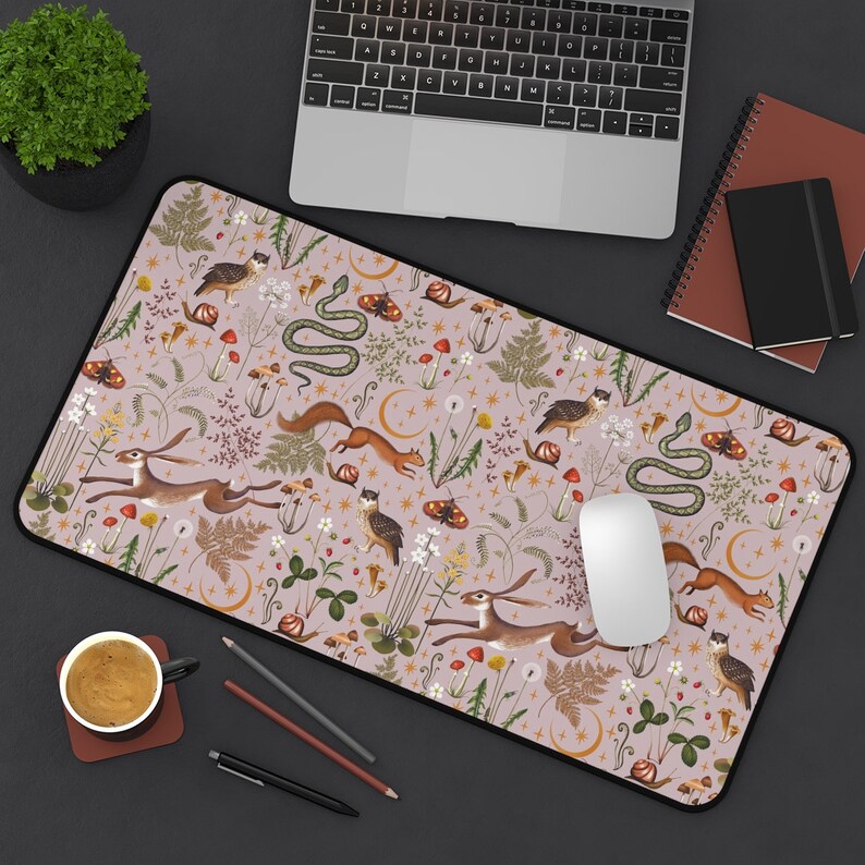 May include: A pink and beige mouse pad with a whimsical woodland design. The design features a variety of animals, plants, and insects, including a snake, a rabbit, a squirrel, and a bird. The mouse pad is perfect for adding a touch of nature to your workspace.