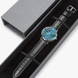 A black leather watch with a colorful floral pattern on the dial, placed in a black box with a silver buckle.