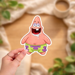 Op de afbeelding: Een sticker met Patrick Star uit Spongebob Squarepants. Het stripfiguur is roze met een groene en paarse korte broek. Hij heeft een wijd open mond met kwijl en een gekke uitdrukking.