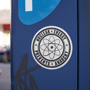 May include: A blue metal parking meter with a white sticker that says "Nuclear Energy Prevents Anarchy" with a black and white atom symbol in the center.