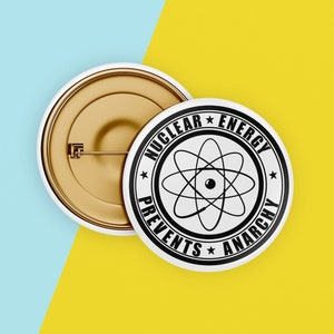 May include: A white button with black text and a black atomic symbol. The text reads "Nuclear Energy Prevents Anarchy".