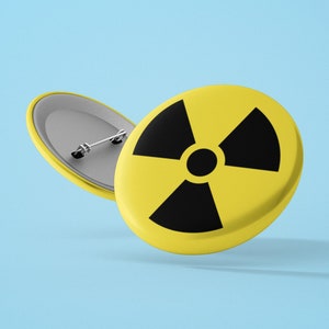 May include: A yellow button with a black radiation symbol. The button has a metal pin on the back.
