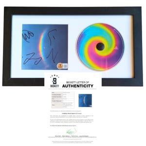 Pode incluir: Encarte de CD do Coldplay emoldurado com um design de arco-íris e assinaturas. O CD é exibido junto com uma Carta de Autenticidade Beckett, tudo dentro de uma moldura preta. O CD tem um padrão de arco-íris vibrante e rodopiante.