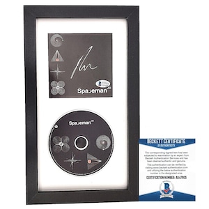 May include: A black framed display featuring a CD and album cover by the band Spaceman. The album cover is black and white with a signature and a Beckett Authentication sticker. The CD is black and white with a Spaceman logo. The Beckett Certificate of Authenticity is visible in the bottom right corner. The certification number is AA47805.