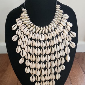 May include: A white cowrie shell necklace with black thread. The necklace is layered and hangs in a waterfall shape.