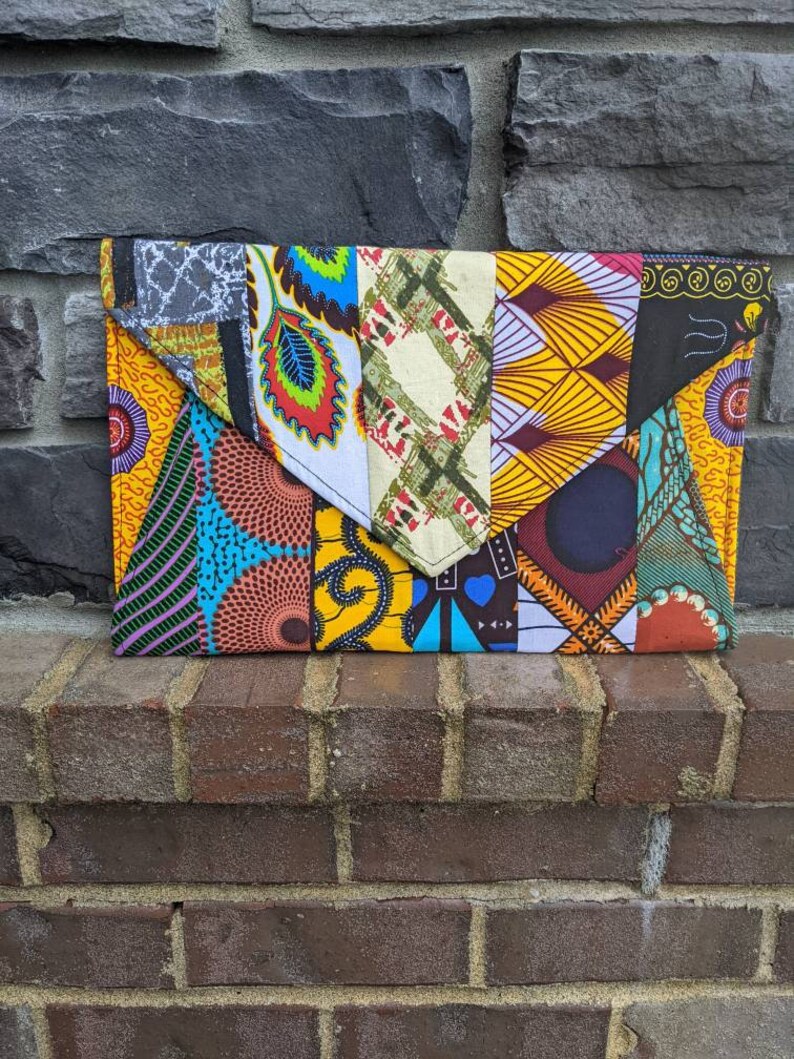May include: A colorful patchwork fabric clutch bag with a variety of geometric and floral patterns in shades of yellow, blue, green, red, and black.