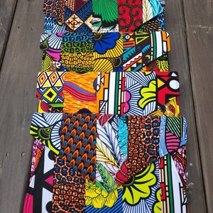 May include: A stack of five colorful fabric clutches with geometric and floral patterns. The clutches are made of a patchwork of different fabrics and are all different colors and designs.
