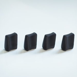 May include: Four black plastic knobs with a slightly curved shape. The knobs are arranged in a row on a white surface.