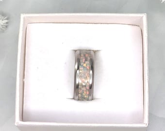 May include: A white ring with iridescent glitter inside a white ring box. The box is on a white surface with white flowers on either side.