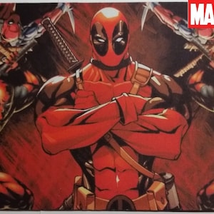 May include: A red and black Deadpool mousepad with a graphic of Deadpool standing with his arms crossed. The background is a red and black abstract design. The text "MARVEL" is in the upper right corner of the mousepad.