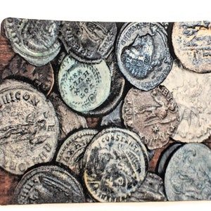 Op de afbeelding: Een verzameling oude, zilverkleurige munten met verschillende ontwerpen en inscripties. De munten zijn willekeurig gerangschikt op een houten oppervlak.