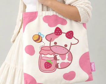 May include: A white canvas tote bag featuring a pink cow print pattern. The center graphic depicts a cartoon cow with a strawberry bow, holding a jar of strawberry jam, accompanied by a small bee. A pink tag on the side reads Bunny Cafe Studio.