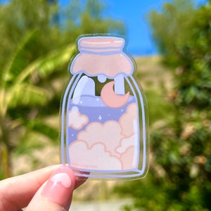 May include: A clear glass jar sticker with a pink moon, white clouds, and blue sky inside. The jar has a pink lid and the text "merryeverything" is visible at the bottom.