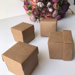 May include: Four small, square, brown cardboard boxes with lids. The boxes are arranged in a semi-circle on a white surface.