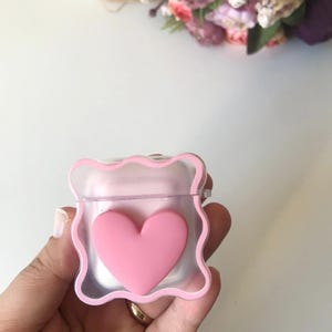 Pode incluir: Uma capa de telefone transparente rosa com um design de coração rosa. A capa tem uma borda ondulada.