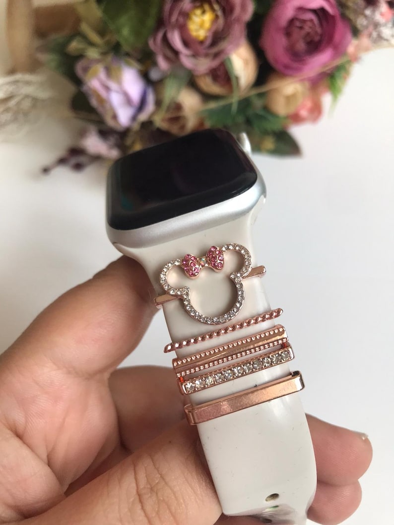 May include: White Apple Watch with a rose gold Minnie Mouse charm and rose gold bands with rhinestones.