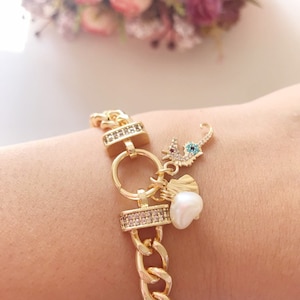 May include: A gold chain bracelet with a charm of a seahorse with a blue evil eye, a white pearl, and a gold charm with clear rhinestones.