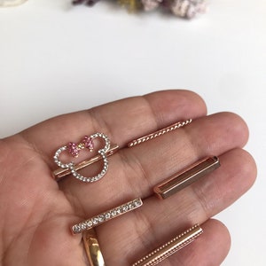 May include: A set of five rose gold-toned metal charms featuring a rhinestone-encrusted Mickey Mouse head with a pink bow, a plain rectangular charm, a rhinestone-encrusted rectangular charm, a plain twisted rope charm, and a beaded rectangular charm.