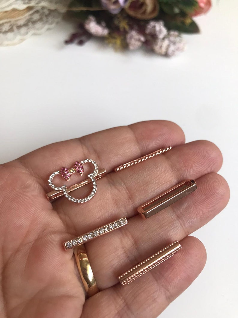 May include: A set of five rose gold-toned metal charms featuring a rhinestone-encrusted Mickey Mouse head with a pink bow, a plain rectangular charm, a rhinestone-encrusted rectangular charm, a plain twisted rope charm, and a beaded rectangular charm.