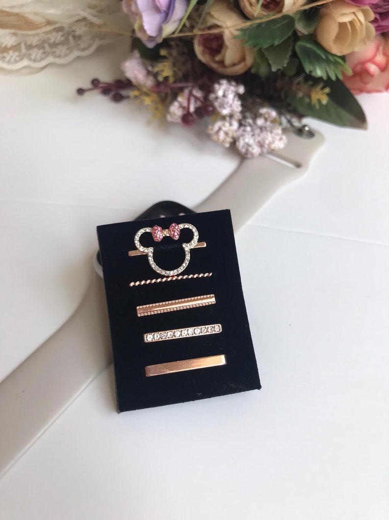 May include: A set of five gold-tone hair clips with rhinestones and a pink bow. The clips are displayed on a black velvet background.