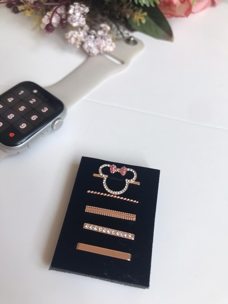 May include: A set of five gold-tone hair clips with rhinestones and a pink bow. The clips are displayed on a black velvet background.