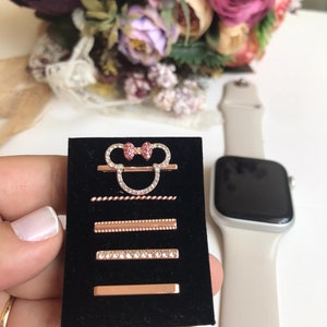 May include: A set of five rose gold watch bands with rhinestones. The bands feature a Mickey Mouse head design with pink bows, a twisted rope design, a beaded design, a row of rhinestones, and a plain band.