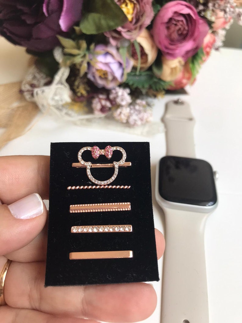May include: A set of five rose gold watch bands with rhinestones. The bands feature a Mickey Mouse head design with pink bows, a twisted rope design, a beaded design, a row of rhinestones, and a plain band.