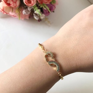 May include: Gold bracelet with a rainbow, cloud, and sun charm. The charm is decorated with colorful cubic zirconia stones.