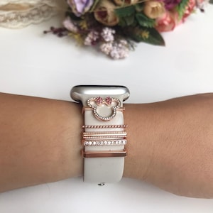 May include: A white silicone Apple Watch band with a rose gold Mickey Mouse charm and four rose gold bands with clear rhinestones.