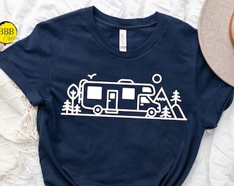 Puede incluir: Una camiseta azul marino con un gráfico blanco de una autocaravana conduciendo por un paisaje de montaña. El gráfico incluye árboles, un sol y un pájaro.