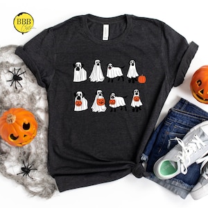 May include: A dark gray t-shirt with a black and white illustration of dogs dressed as ghosts for Halloween. The dogs are holding pumpkins and some are wearing ghost costumes.