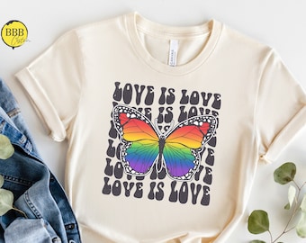 May include: A beige t-shirt with a rainbow butterfly graphic and the text "Love is Love" repeated in a retro font.